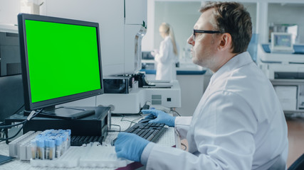 Male Research Scientist Sits at His Workplace in Laboratory, Uses Green Mock-up Screen Personal...