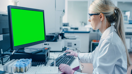 Female Research Scientist Sits at His Workplace in Laboratory, Uses Green Mock-up Screen Personal...