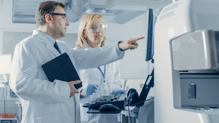Two Research Scientists Programm Medical Equipment with Tablet Computer. Male Doctor Points the...