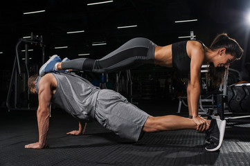 Fototapeta na wymiar Sport, fitness, yoga, couple and teamwork concept. Young man and woman doing double plank exercises in gym. Copy space.