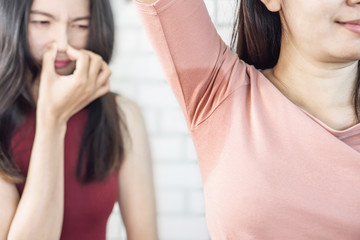 Asian woman having problem sweat under armpit  with friend smelling stink in background 