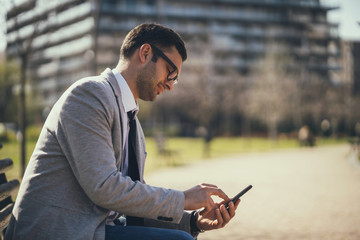 Fototapeta premium Young businessman is using smartphone in park.