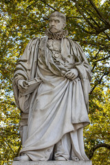 Statue of Michel de Montaigne in public garden along Place des Quinconces, Bordeaux France, with a canopy of green trees.