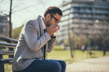 Young businessman is having allergy. He is blowing nose.