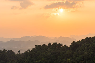 Beautiful orange sunset in Asian jungle with misty outlines of mountains in the distance