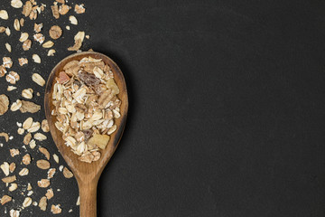 Scattered muesli and wooden spoon with copy space on black plate. Top view