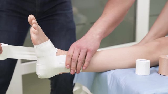 A therapist fixing sport tape on patients ankle. Tibia joint taping. Sport and rehabilitation concept