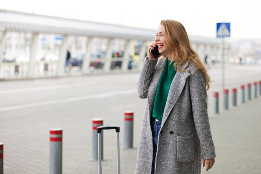  Smiling woman talking on the phone near the airport terminal. Beautiful lady emotionally talking on the phone. Happy positive girl with smartphone