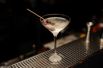 Cocktail in the ice cold glass decorated with a berries on the skewer on the bar counter