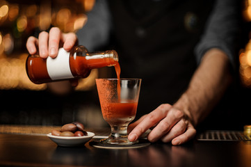 Professional bartender pouring a prepared Bloody Mary cocktail from the bottle to the glass decorated with red powder
