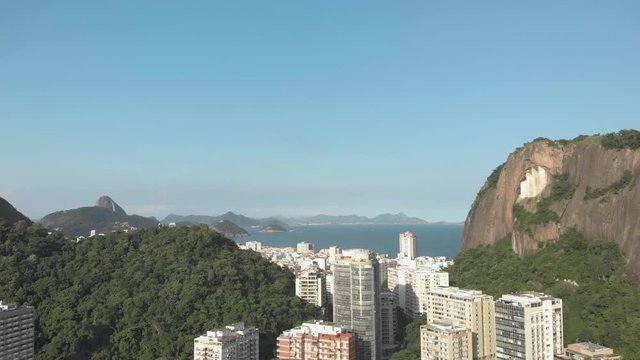 Slow aerial movement forward with view of high rise residential buildings among rocky mountain hills with in the background the neighbourhood of Copacabana with the Sugarloaf mountain