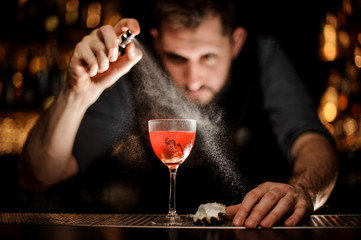 Professional bartender spraying on the delicious transparent red cocktail in the glass