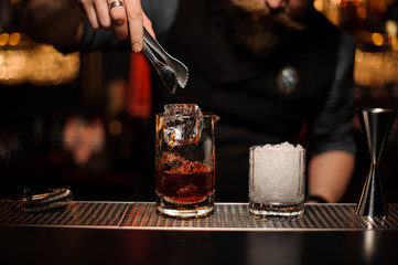 Bartender throwing to a cocktail glass an ice cube with tweezers