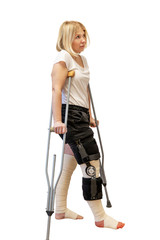 Young woman after knee surgery. On crutches, in an orthosis and with bandaged legs. Isolated on a white background. Vertical.