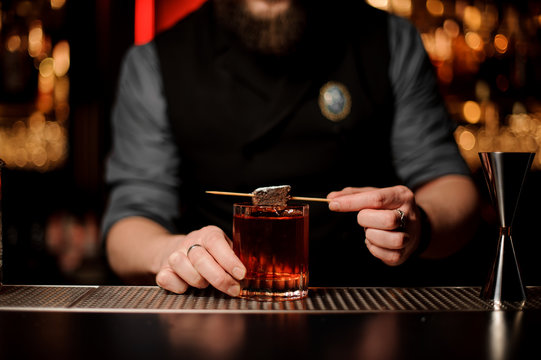 Professional male bartender adding a brownie piece on the skewer with powdered sugar to a cocktail glass
