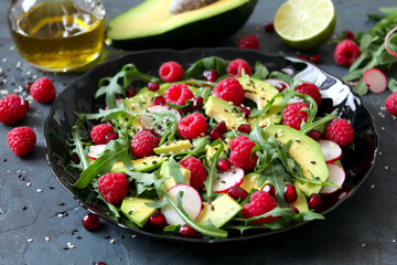 Avocado salad with raspberries, pomegranate, arugula and sesame on dark background. Top view with copy space. Healthy food.