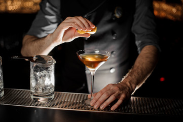 Professional bartender adding to a cocktail in the glass a juice from a lemon zest
