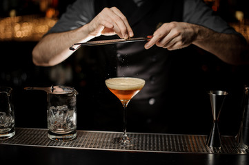 Professional bartender adding to a cocktail in the glass a grated nutmeg