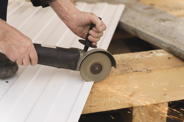 Construction worker sawing steel sheet with trapezoidal profile during roofing works