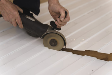 Construction worker sawing steel sheet with trapezoidal profile during roofing works