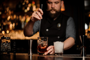 Bartender stirring alcohol with an ice cubes in the tall measuring glass cup with a spoon