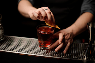 Bartender adding to a cocktail in the glass a orange zest as a decor