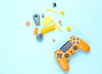 Children's 80s entertainment on blue background. Orange gamepad, children's constructor bricks, top view, minimalism.