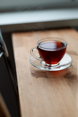A glass cup of hot black tea on the wooden table. Breakfast concept.