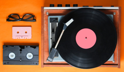 Retro style,80s, pop culture attributes on orange background. Vinyl player, 3D glasses, audio, video cassette. Top view
