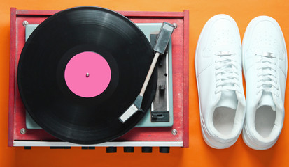 Pop culture. White hipster sneakers, vinyl player on orange background. Retro style. 80s. Top view, minimalism
