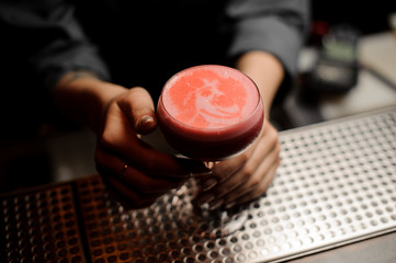 Bartender serving a smooth crimson cocktail in the glass with a silhouette as a decor
