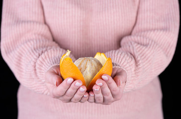 Peeled orange on the palms of a girl in a pink sweater.