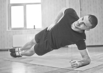 Healthy Sporty Man Doing Indoor Side Plank Exercise on Mat, Static Exercise. Black and white.