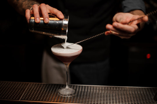 Professional bartender pouring a whipped cream to the cocktail glass on the spoon