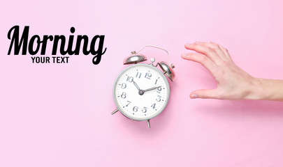 Female hand takes alarm clock on pink background. Top view. Time to wake up. Morning, copy space...