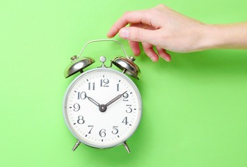 Female hand takes alarm clock on green background. Top view. Time to wake up. Minimalism.