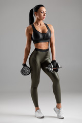 Fitness woman with dumbbells on gray background. Muscular woman workout