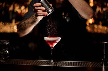 Professional bartender adding to a cocktail with a whipped cream a red powder in the dark