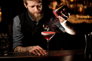 Professional bartender with a beard adding to a cocktail with a whipped cream a red powder