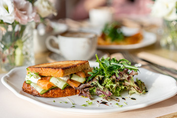 French toast brioche, Sandwich with salmon and cucumber. Light morning Breakfast, fresh warm pastries and aromatic cappuccino coffee on table in restaurant