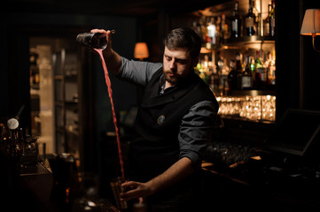 Fototapeta na wymiar Bartender with a beard making cocktail in the steel shaker