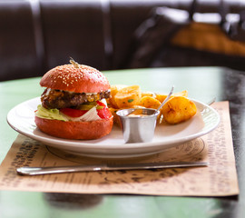 on a white plate, a meat burger with onion, tomato, lettuce and a pickled cucumber