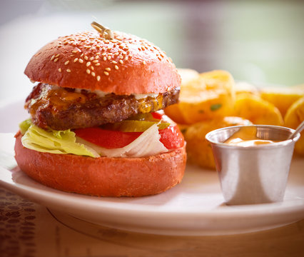 on a white plate, a meat burger with onion, tomato, lettuce and a pickled cucumber