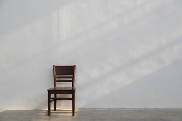 single brown wooden chair with light ray from window on white wall background.