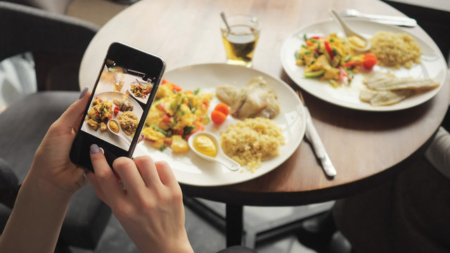 Woman blogger takes photos of her food in a cafe using mobile phone. Hands with phone screen close-up.