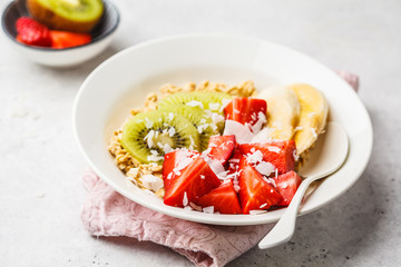 Summer oatmeal with fruit and coconut in white plate.