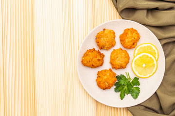 Homemade red fish cakes with lemon and parsley in ceramic plate. With fabric drapery on wooden background, copy space, top view.