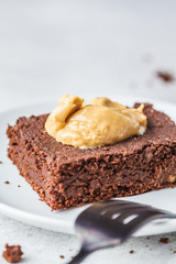 Piece of vegan chocolate brownie with peanut butter on white plate.