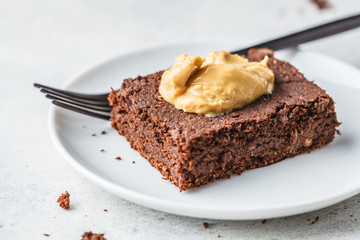 Piece of vegan chocolate brownie with peanut butter on white plate.