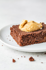 Piece of vegan chocolate brownie with peanut butter on white plate.